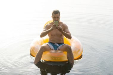 Sudaki şişme bir halkası üzerinde siting ve bir sm tutan bir adam