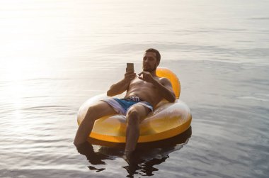 Sudaki şişme bir halkası üzerinde siting ve bir sm tutan bir adam