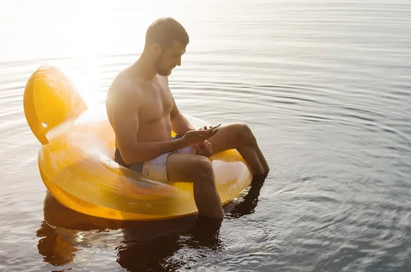 En man placering på en uppblåsbar ring i vattnet och hålla en sm — Stockfoto