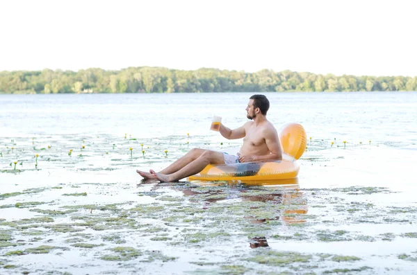 En man dricker öl sitter i en gummiring i vattnet, gratis sp — Stockfoto