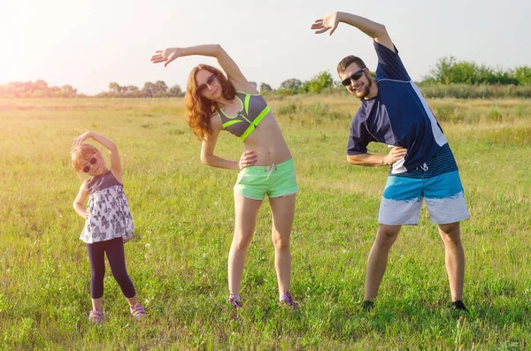 Happy young family doing exercises outdoors. Mom, Dad and daught