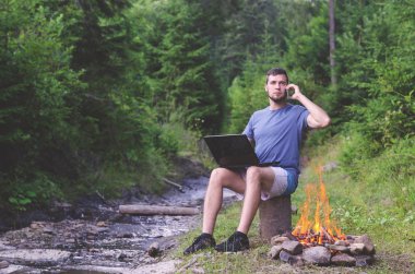 C açık havada, çalışan bir smartphone üzerinde konuşurken bir dizüstü bilgisayar ile bir adam