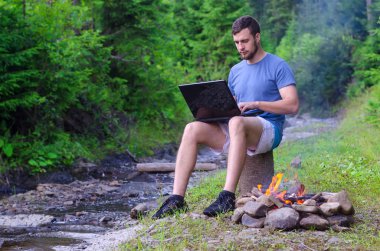 Bir mountain yakınındaki bir ormandaki bir dizüstü bilgisayar üzerinde çalışan işadamı rive