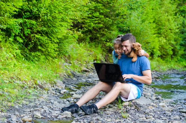 Papá y su hija están mirando el portátil, sentados en el natur — Foto de Stock