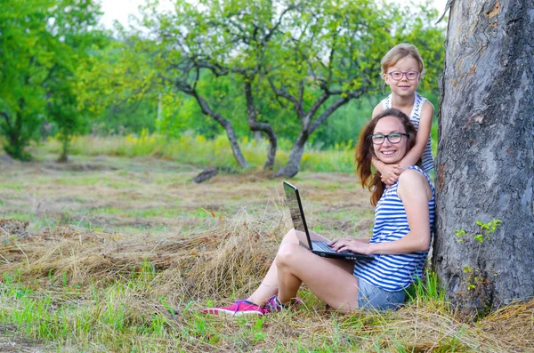 Happy family: mother and daughter working on a laptop in nature,