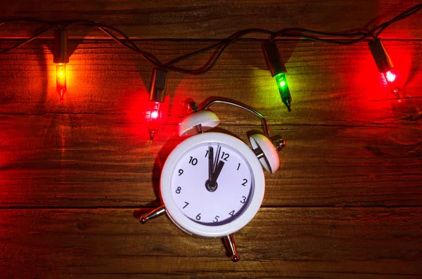 New Year's lights and clock on a wooden table, top view. — Stock Photo, Image