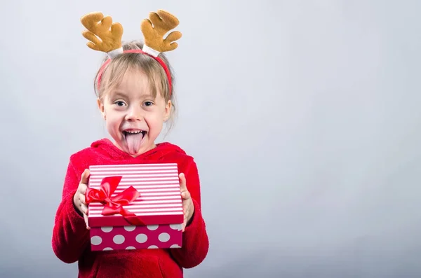 Cute little girl in a deer costume is holding a christmas gift, — Stock Photo, Image
