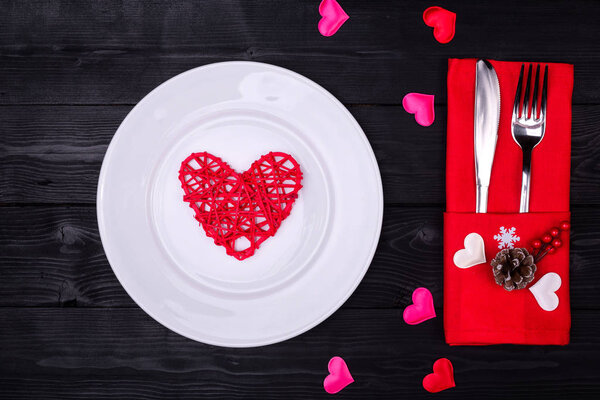 День святого Валентина стол накрыть вилкой, ножом, тарелкой и красной салфеткой ужин на черном фоне
.