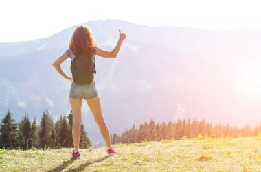 Genç kadın bir sırt çantası ile dağın tepesinde duruyor ve 