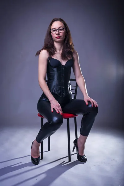 Sexy jonge vrouw in een korset en de latex op een stoel. — Stockfoto