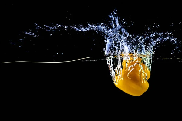 Färsk gul paprika i vatten stänk på en svart bakgrund. — Stockfoto