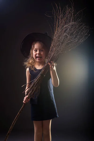 Küçük kız cadı şapka ve koyu bir arka plan afiş Cadılar Bayramı için ellerinde süpürge. — Stok fotoğraf