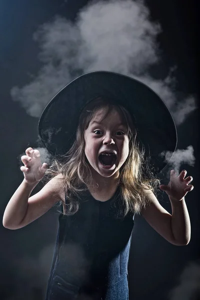 Duman karanlık bir arka plan üzerinde cadı şapkalı güzel kız. — Stok fotoğraf