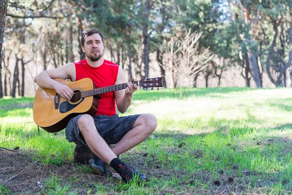 Jonge, bebaarde man een akoestische gitaar spelen, buiten. — Stockfoto