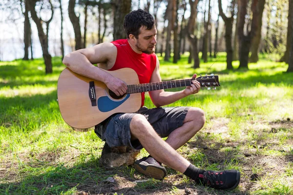 Jonge, bebaarde man een akoestische gitaar spelen, buiten. — Stockfoto
