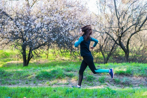 Mujer joven en una mañana correr a través del bosque de primavera . — Foto de Stock