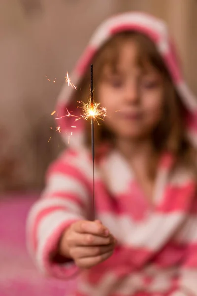 Glückliches kleines Mädchen blickt mit Bewunderung auf brennende Wunderkerze in ihrer Hand über. — Stockfoto