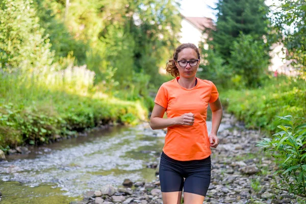 Chica en una camiseta naranja brillante corriendo a lo largo de un río de montaña . — Foto de Stock