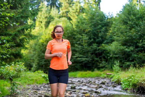 Chica en una camiseta naranja brillante corriendo a lo largo de un río de montaña . —  Fotos de Stock
