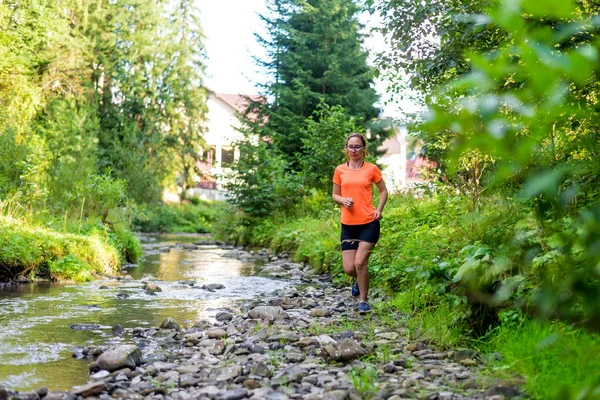 Chica en una camiseta naranja brillante corriendo a lo largo de un río de montaña . — Foto de Stock