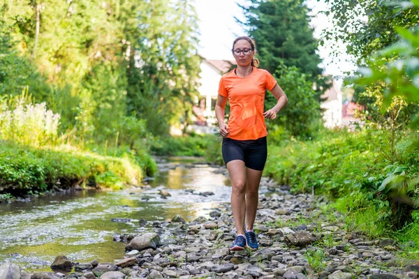 Chica en una camiseta naranja brillante corriendo a lo largo de un río de montaña . — Foto de Stock