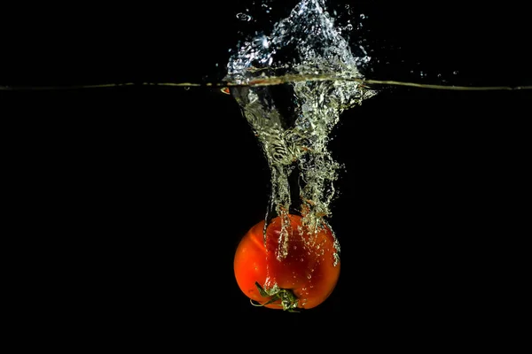 Pomodoro fresco caduto in acqua, isolato su fondo scuro — Foto Stock