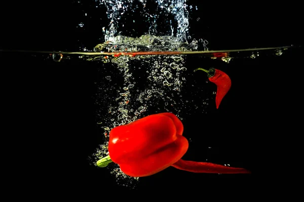 Red fresh paprika and chili pepper splash in water on a black background. — Stock Photo, Image