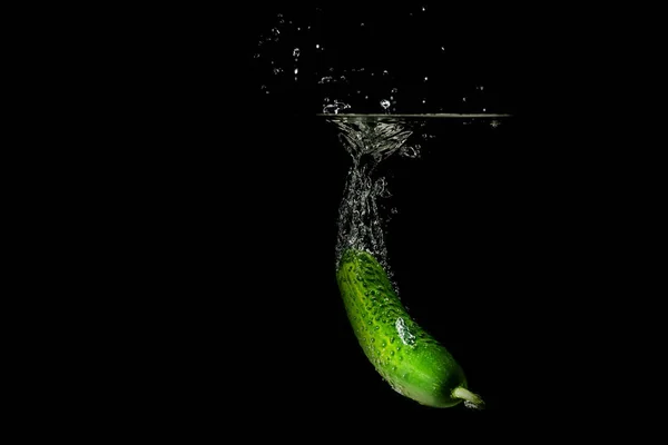 Fresh green cucumber in water with splash on black background