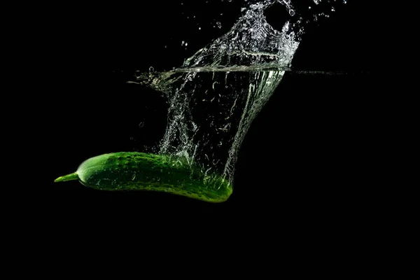 Свіжий зелений огірок у воді з бризкою на чорному тлі — стокове фото