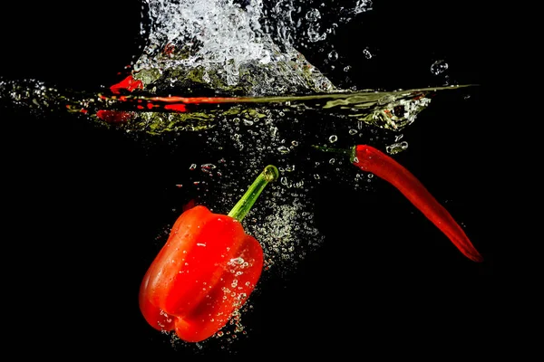 Pimentón rojo fresco y chile salpicado en agua sobre un fondo negro . — Foto de Stock