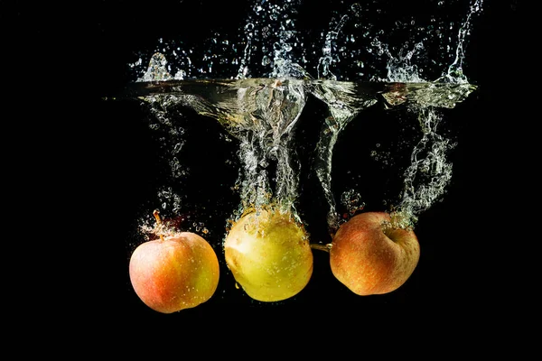 Τρία μήλα βυθίζονται στο νερό σε μαύρο φόντο. — Φωτογραφία Αρχείου