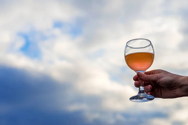 Un vaso con una bebida en la mano de una mujer contra el cielo, espacio libre . — Foto de Stock