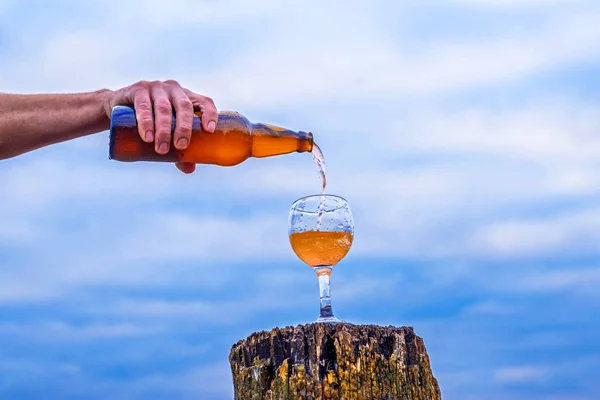 Una mano masculina vierte una bebida en un vaso sobre el fondo de un hermoso cielo . — Foto de Stock