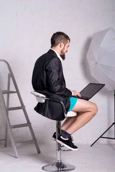 Man in a jacket and shorts is sitting with a laptop, the concept of remote work. Workaholic works from home. Freelance.