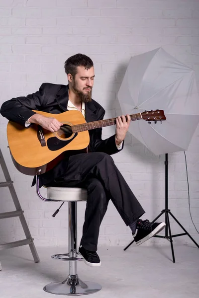 A man in a shirt and jacket with an acoustic guitar. Bearded guitarist.