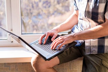 İş adamı pencere eşiğinde otururken dizüstü bilgisayarla çalışıyor. Uzaktan kumanda konsepti. Kendini soyutlama. Çok çalışkan. Evde çalış. Ev yalıtımı.