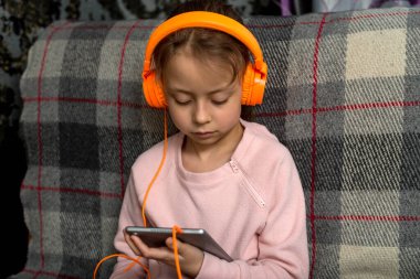 Sevimli birinci sınıf öğrencisi kulaklıkla oturuyor ve kanepede bir tabletle oturuyor. Karantina sırasında uzaklık öğrenme kavramı.