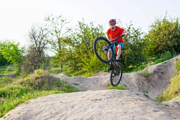 Professional cyclist in a bright T-shirt performs a jump. Extreme sport. Cyclist on a mountain bike.