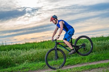 Bisikletin ön tekerleğinde duran kasklı bir bisikletçi. Aşırı bisiklet konsepti. Hile.