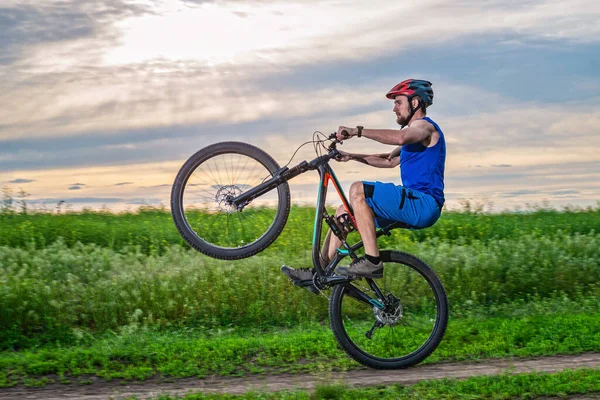 Rowerzysta Kasku Jeździ Rowerze Tylnym Kole Podczas Zachodu Słońca Kołyska — Zdjęcie stockowe
