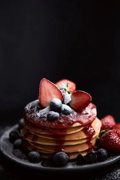 Pfannkuchen aus nächster Nähe, mit frischen Erdbeeren, Blaubeeren, Minze und Marmelade auf schwarzem Hintergrund — Stockfoto