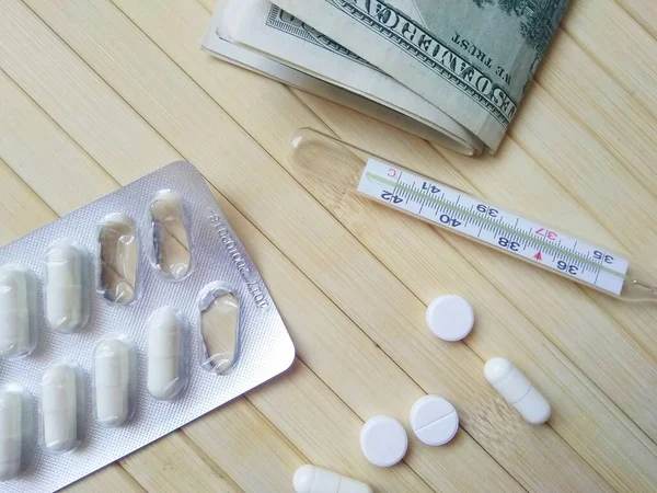 pills with money and thermometer on wooden background