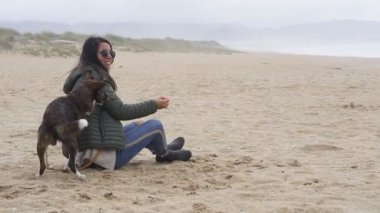 Kız kumsalda köpekle oynuyor ve eğleniyor. Ağır çekimde tek başına.