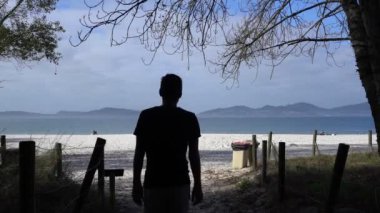 Beyaz bir adam İspanya 'da arka planda dağları olan beyaz bir kumla kumsala yürüyor.