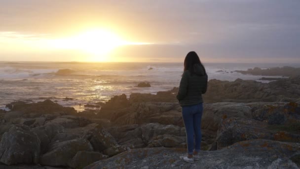 美しい夕日の岩のビーチの風景を見ている女性波がスペインの大西洋をクラッシュして穏やかなリラックス — ストック動画