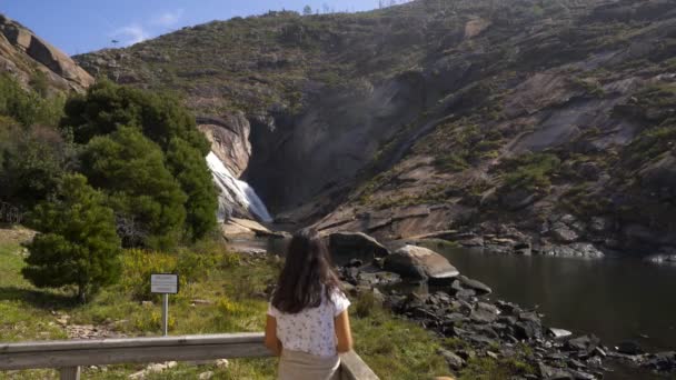 スペインの岩の間の湖に墜落したエザロの滝の水を見ている女の子の旅行者 — ストック動画