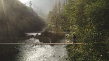 Fragas do Eume, İspanya 'da vahşi bir ağaç manzarasında köprüdeki bir adamın insansız hava panoramik görüntüsü.
