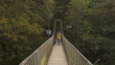 Köpeği olan bir kadın Fragas do Eume, İspanya 'daki ağaçlar arasındaki bir nehrin üzerindeki orman manzarasında köprüden geçiyor.