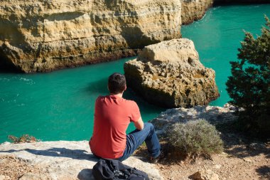 Portekiz, Algarve 'de turkuaz suyu olan gizli, vahşi bir sahile bakan bir adam.