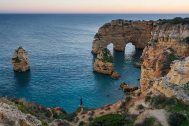 Praia da Marinha sahilinin doğal kemer kayalıklarında kadın gün batımında Atlantik okyanusuyla güzel bir manzara, Lagoa Portekiz 'de